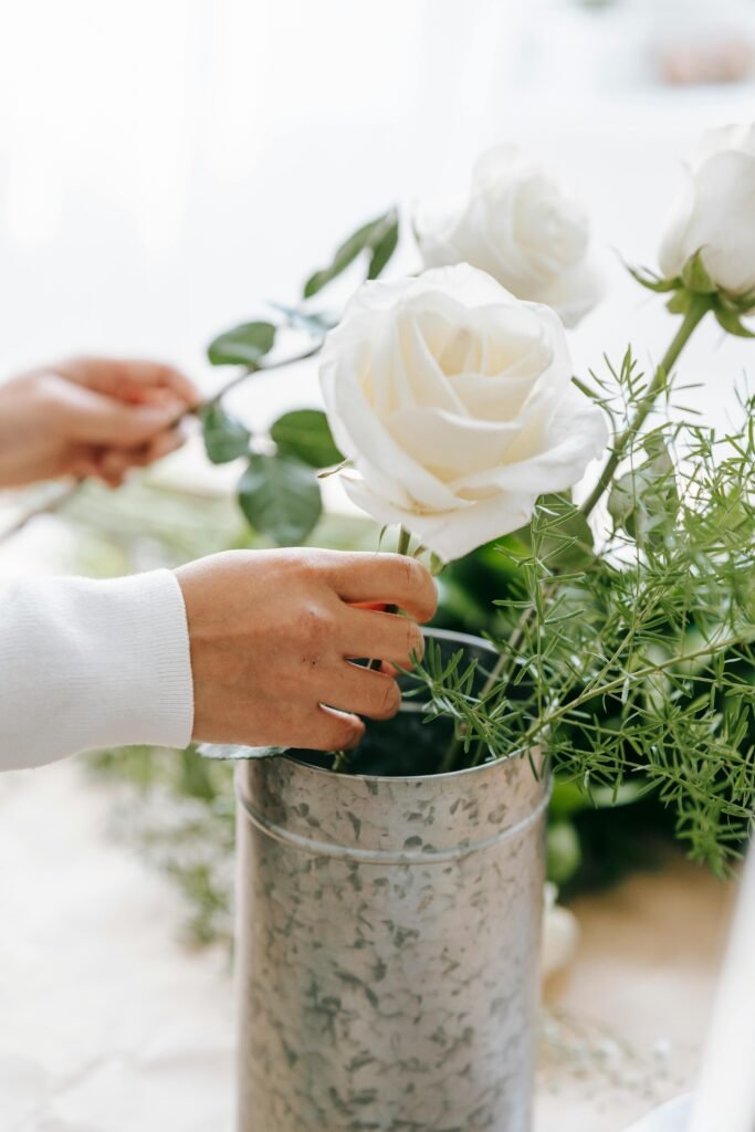 A young adult arranges a white rose bouquet in a decorative vase indoors.