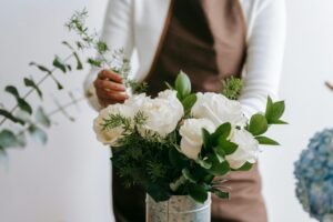 A florist delicately arranges a fresh white rose bouquet in a metal vase, indoors.