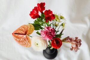 Top view of a colorful flower arrangement in a black ceramic vase on a white fabric background.